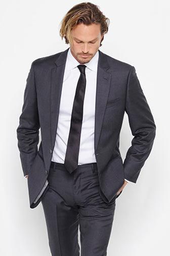 man wearing dark gray suit walking with hands in pants pockets
