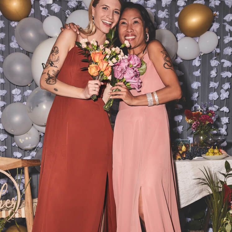 2 bridesmaids wearing red and pink dresses holding flower bouquets standing next to each other