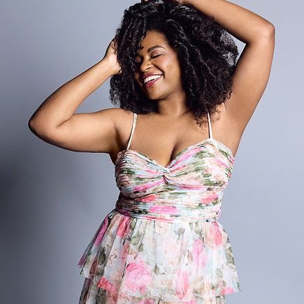woman in floral print dress smiling with her hands on her head