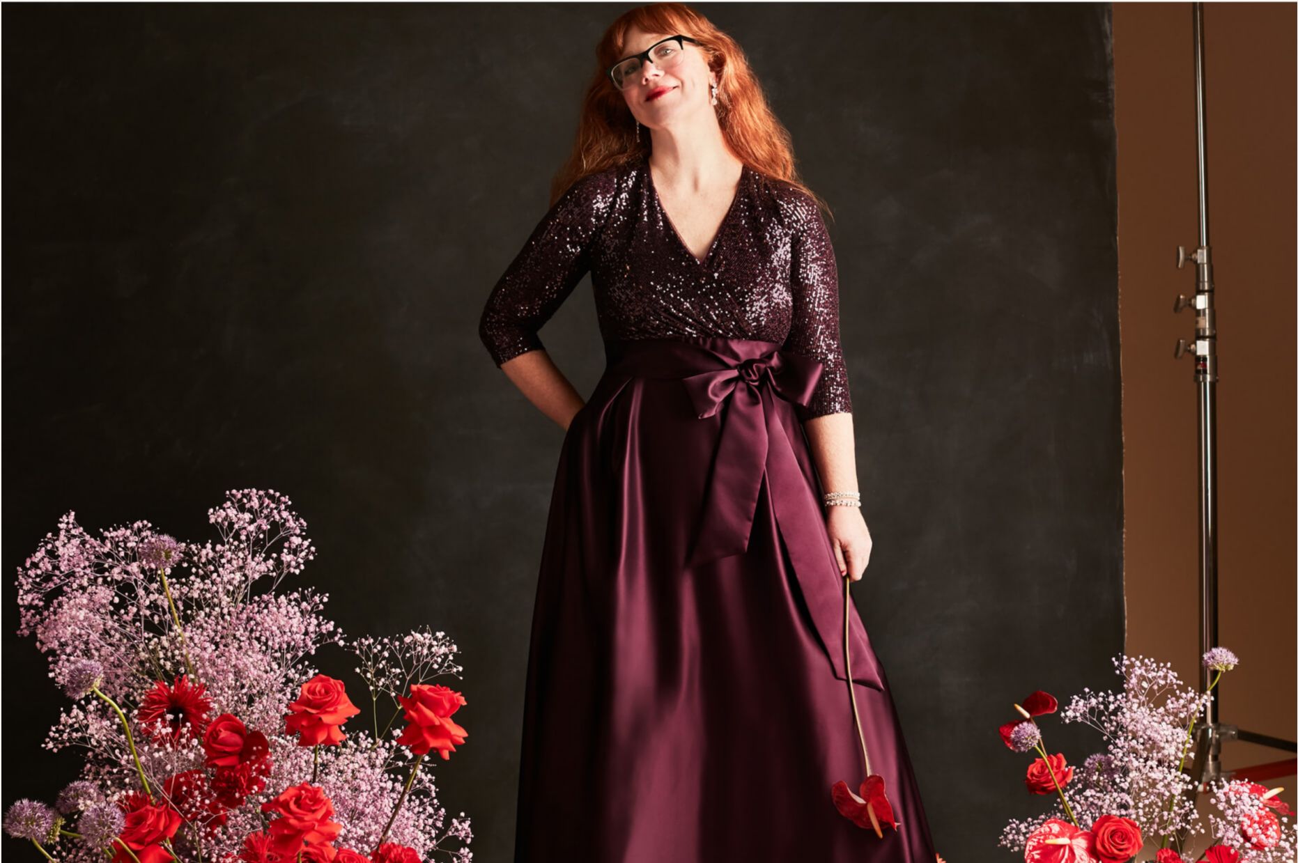 woman in a purple dress standing next to flower bouquets in front of a gray backdrop