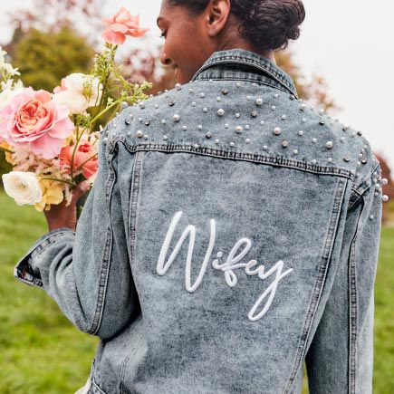 closeup of bride wearing a wifey jean jacket and holding a bouquet