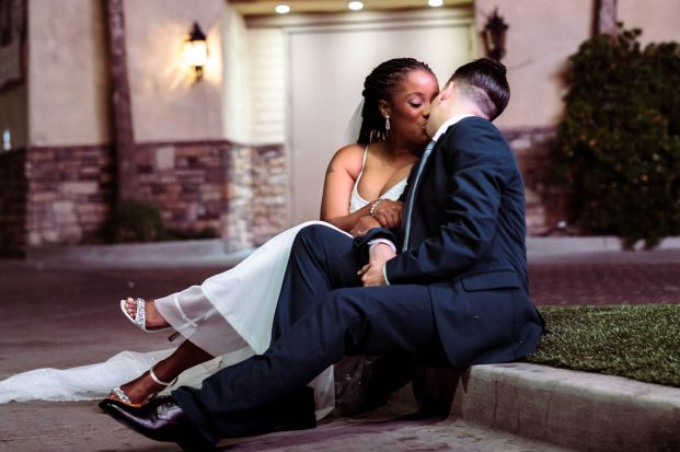 bride and groom sitting on a curb outside kissing