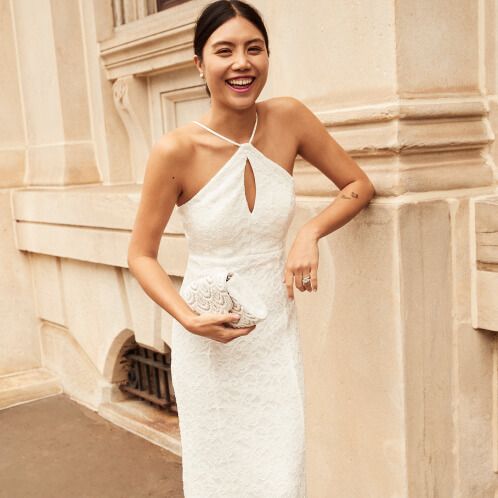 laughing bride holding a handbag and leaning against a building