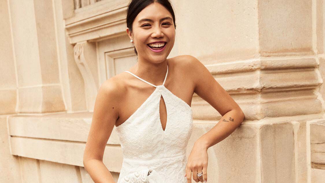 bride in dress smiling and standing next to a building