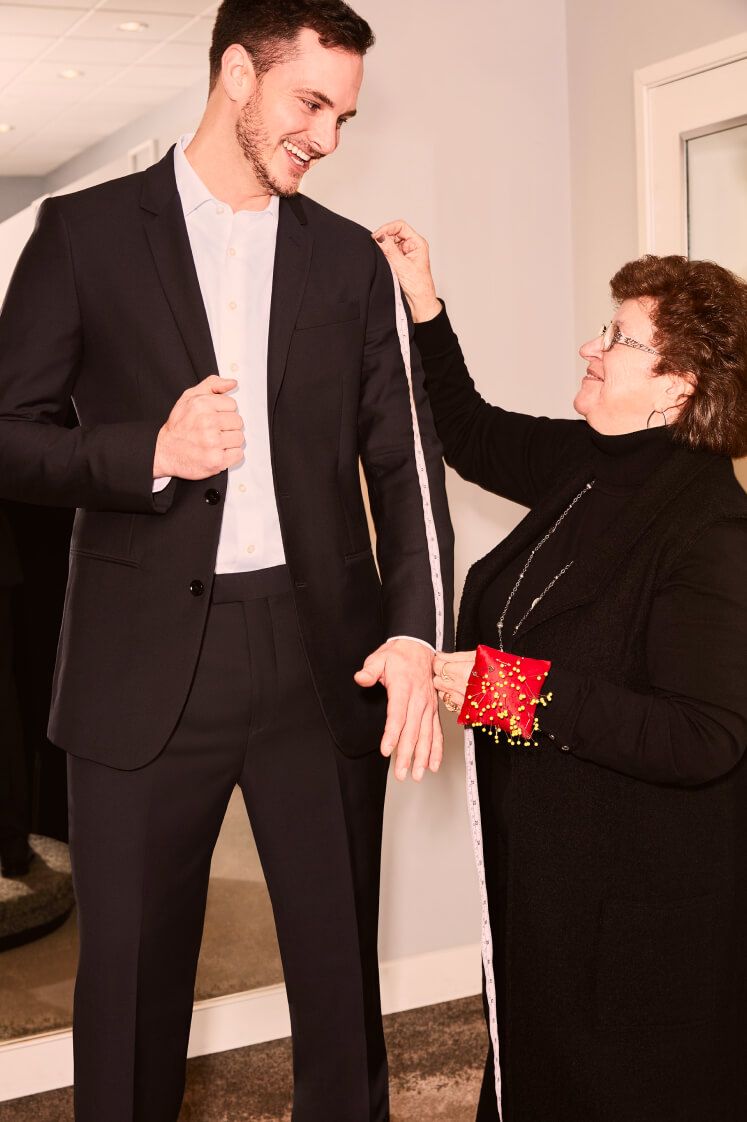 groom in a black tuxedo getting jacket measured by a store associate