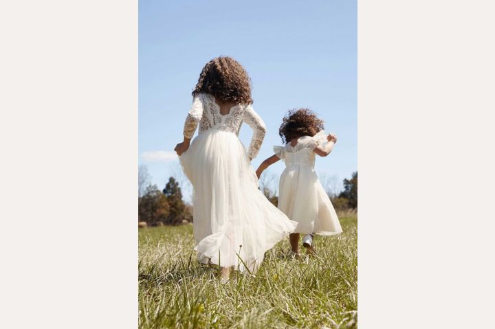 backs of two flower girls running in a field