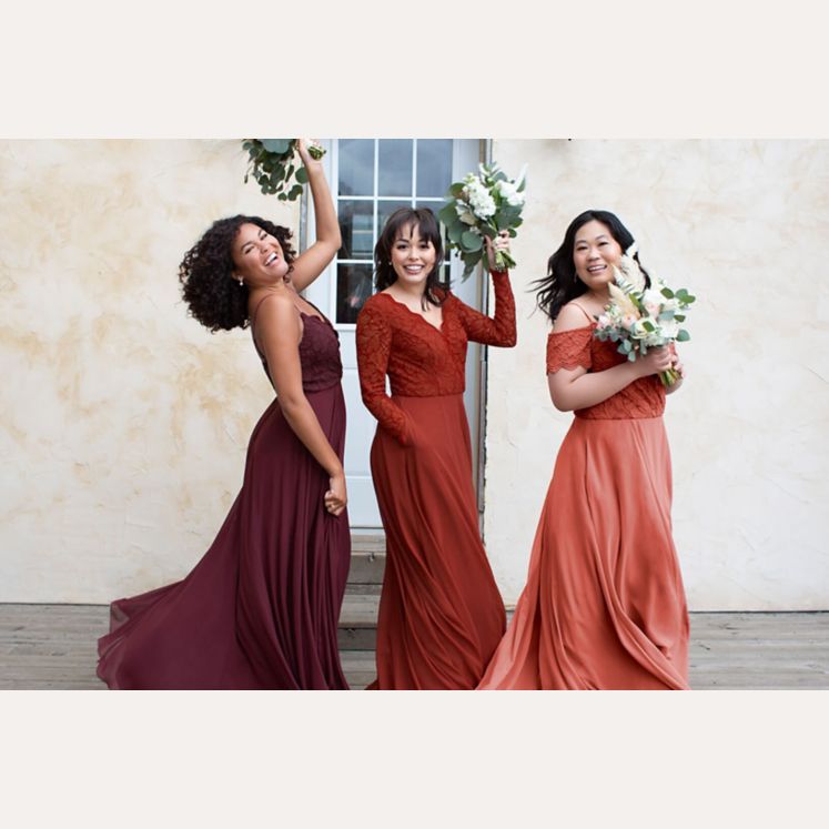 3 bridesmaids in purple, orange, and red dresses standing and holding bouquets