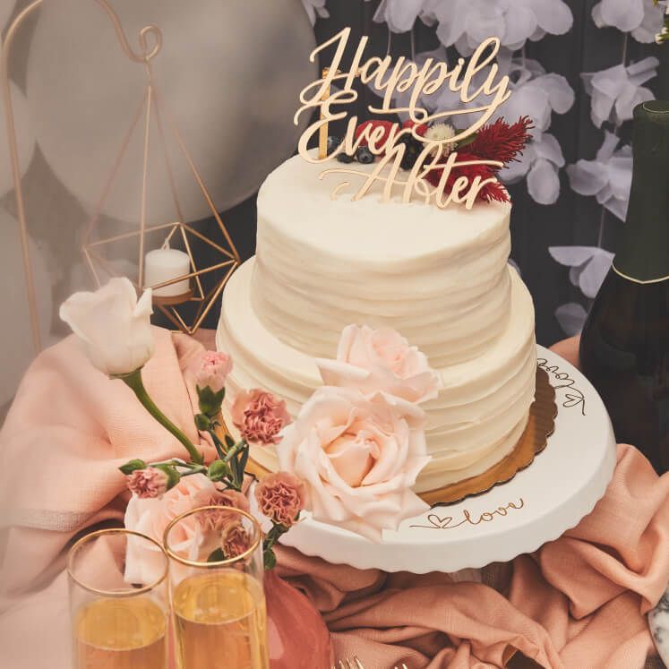 wedding cake with happily ever after cake topper next to champagne glasses and roses on a table