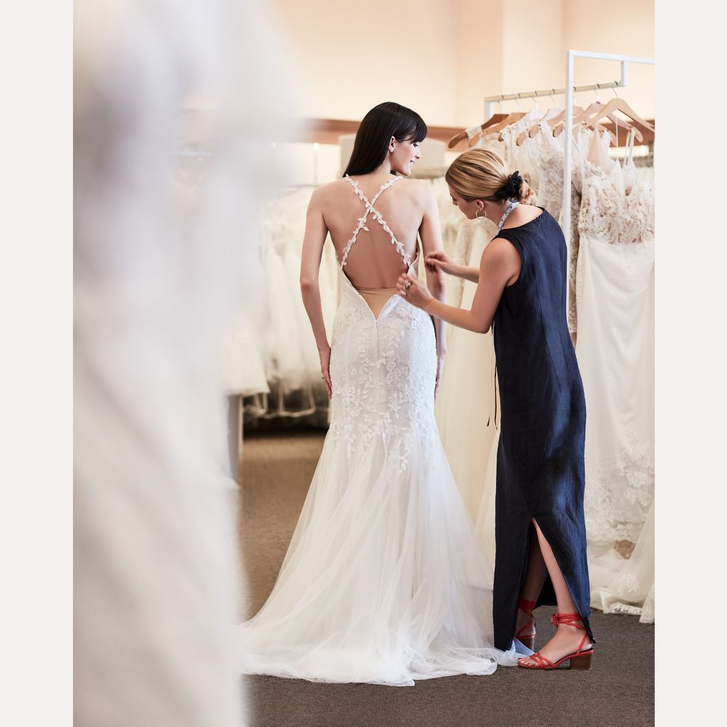 store associate helping bride with wedding dress fitting