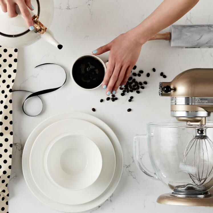 hands making coffee with coffee cup, coffee beans, rolling pin, and blender laid out on a table