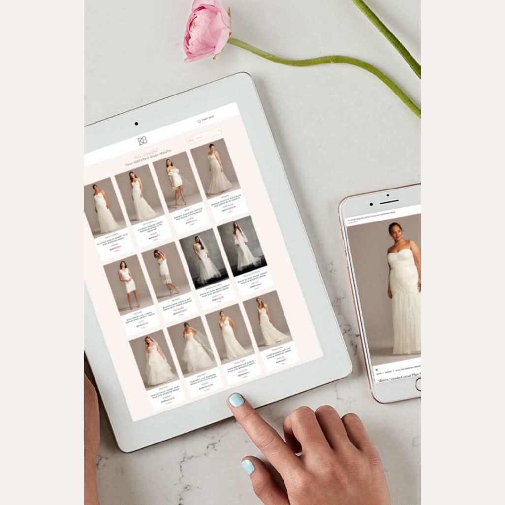 hands on an ipad showing wedding dresses next to a cell phone, and flower on a table