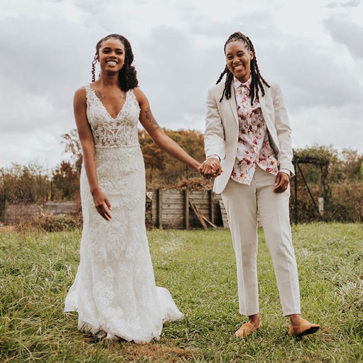 bride in a wedding dress and a groom in a suit holding hands and walking in a grass field
