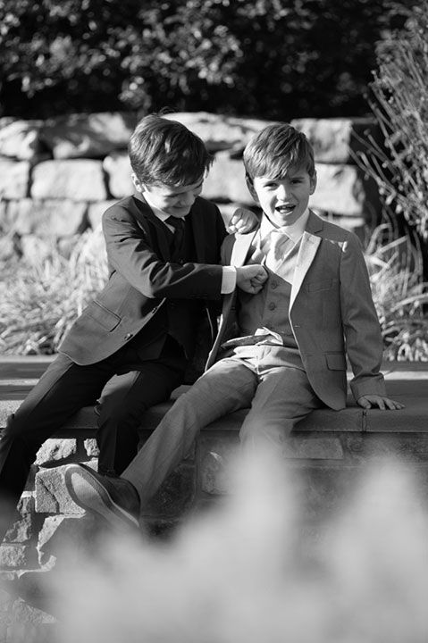 two boys wearing tuxedos sitting on a bench together