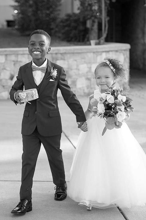ring bearer wearing a tuxedo holding hands with flower girl wearing a dress