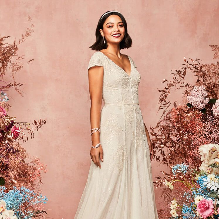bride in a cap sleeve wedding dress standing next to floral arrangements