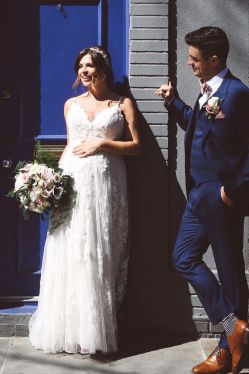 pregnant bride in dress standing with groom in blue suit