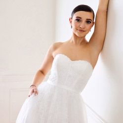 woman in wedding dress with her arm abover her head leaning on a wall