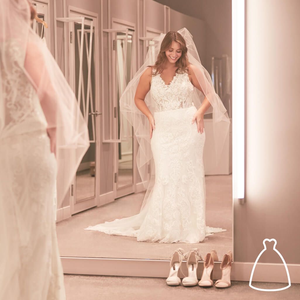 bride wearing a wedding dress and veil looking into a mirror at a store