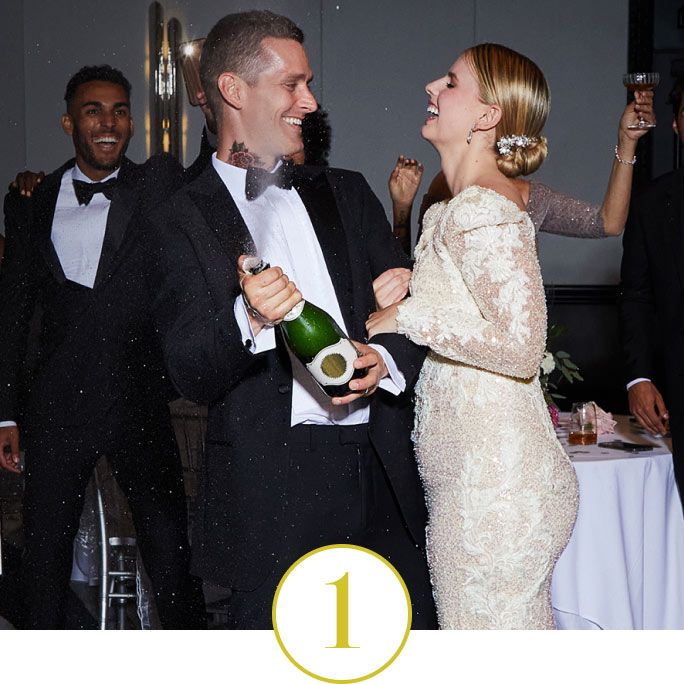 bride and groom with their party popping a bottle of champagne