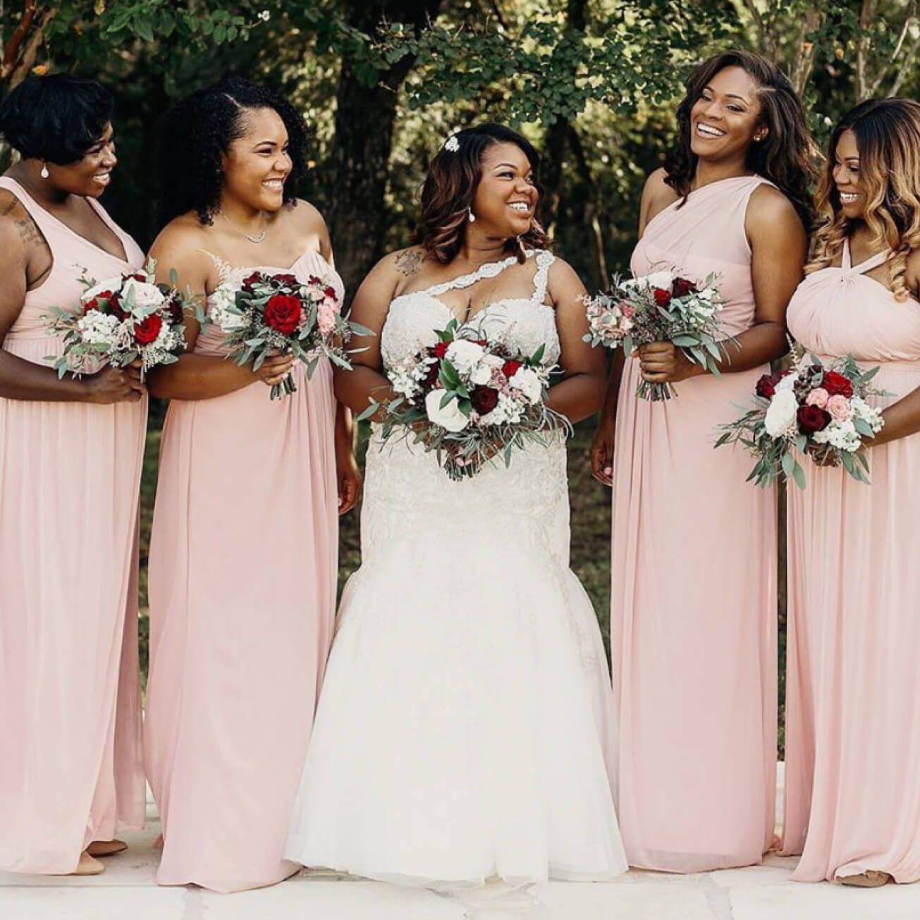 bride in a wedding dress standing with bridesmaids in different pink dresses holding flower bouquets