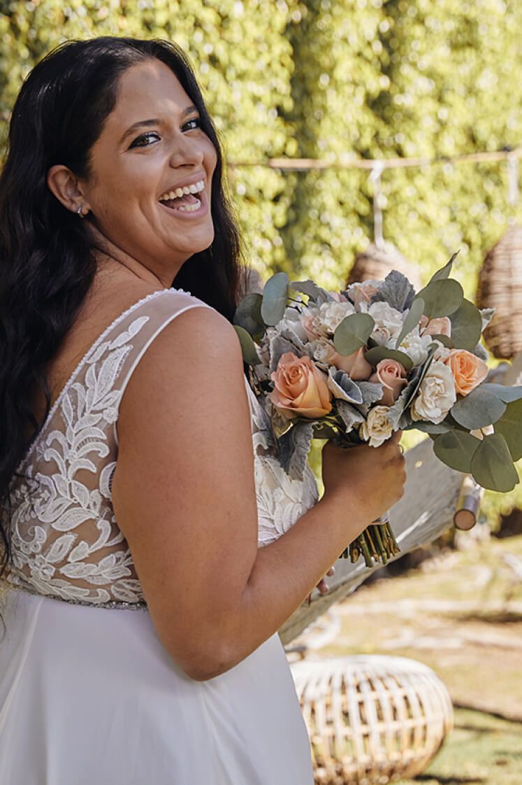 smiling bride in a wedding dress holding a bouquet of orange, pink, and white roses