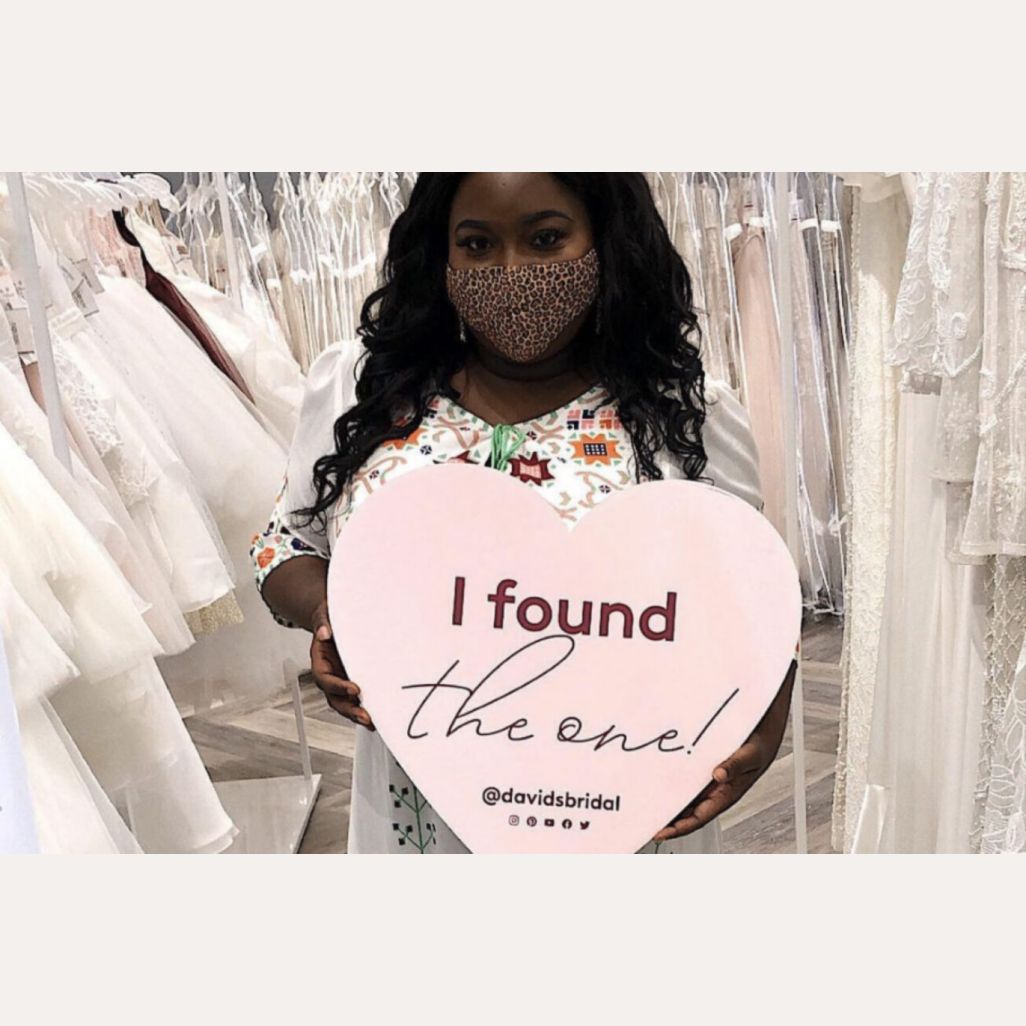 woman wearing a mask holding a heart shaped sign in a store