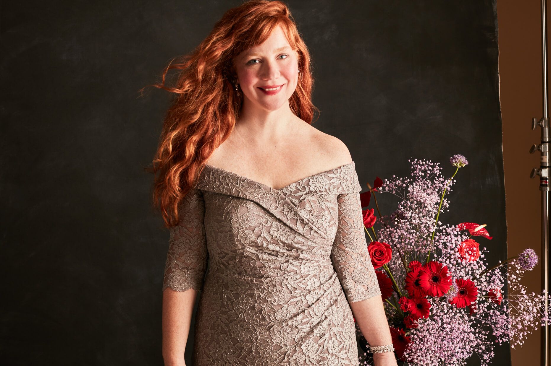 woman in a gray off-the-shoulder dress standing in front of a flower bouquet