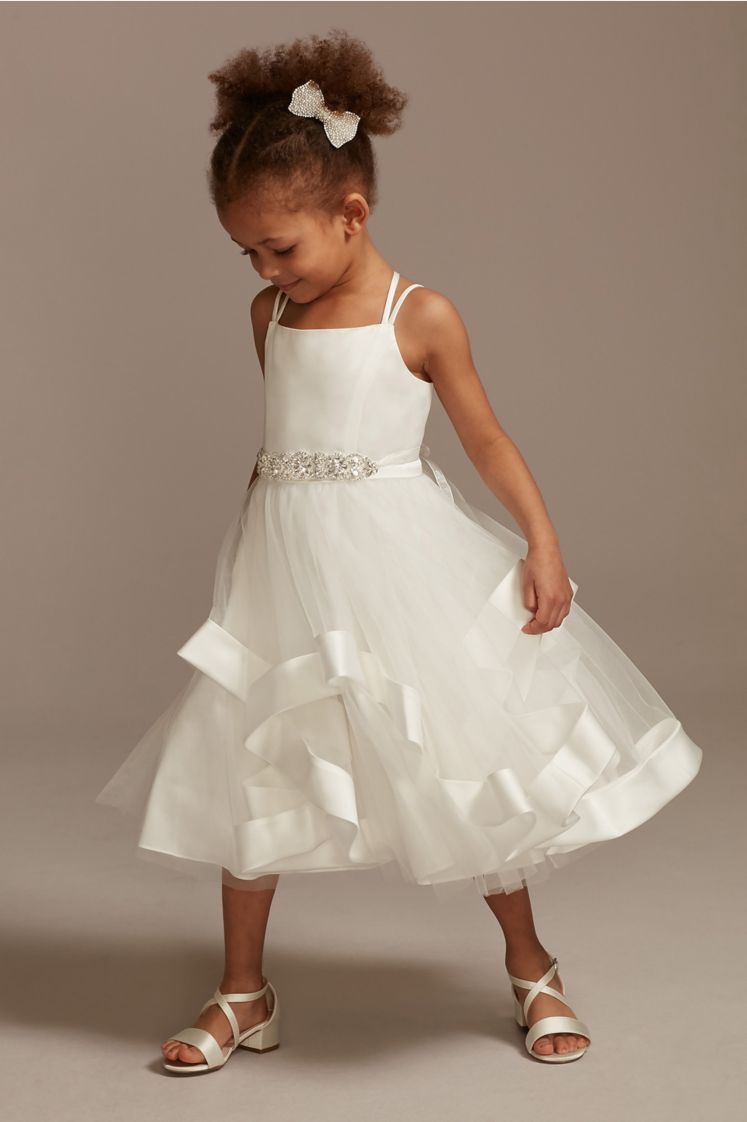 flower girl in a sleeveless satin dress wearing a hair bow looking down to the ground