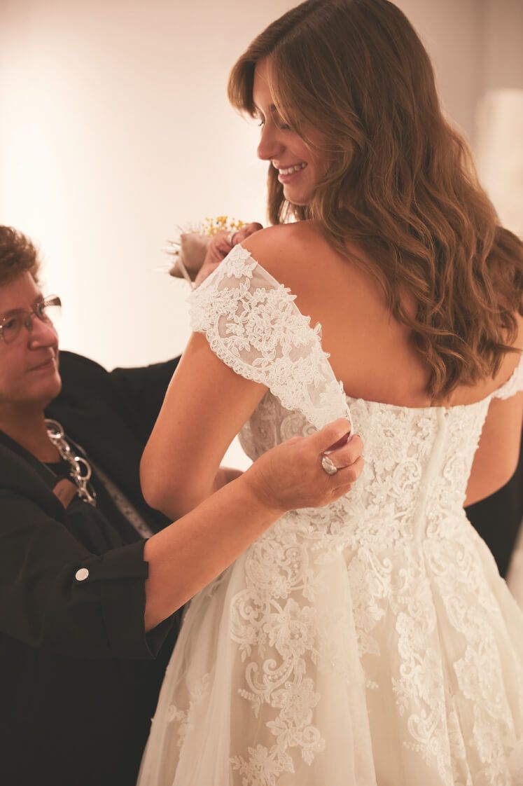 store associate helping bride with the fitting of a sleeve on the back of wedding dress