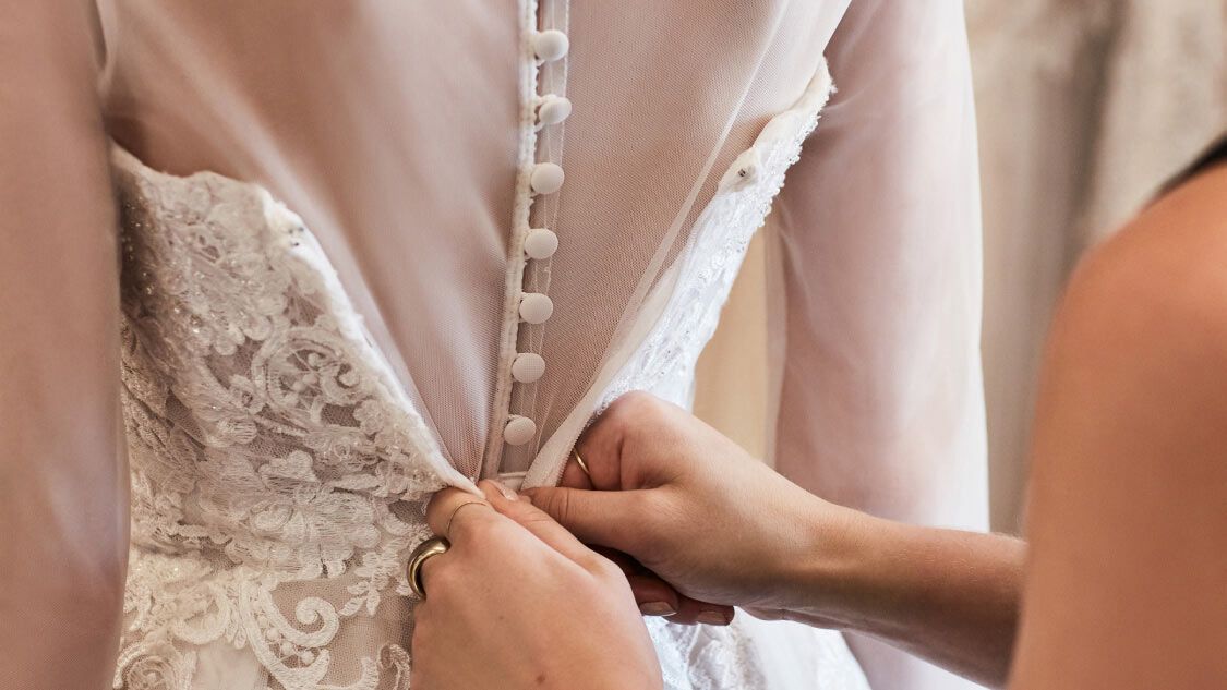 store associate helping bride with wedding dress fitting