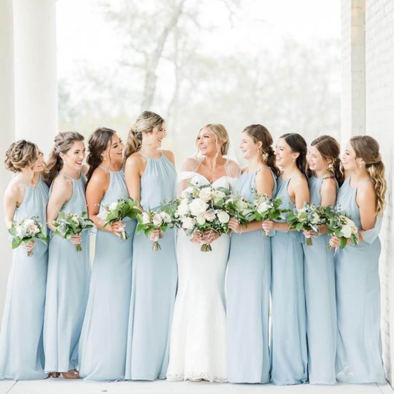bride in a wedding dress standing with bridesmaids in blue dresses holding flower bouquets