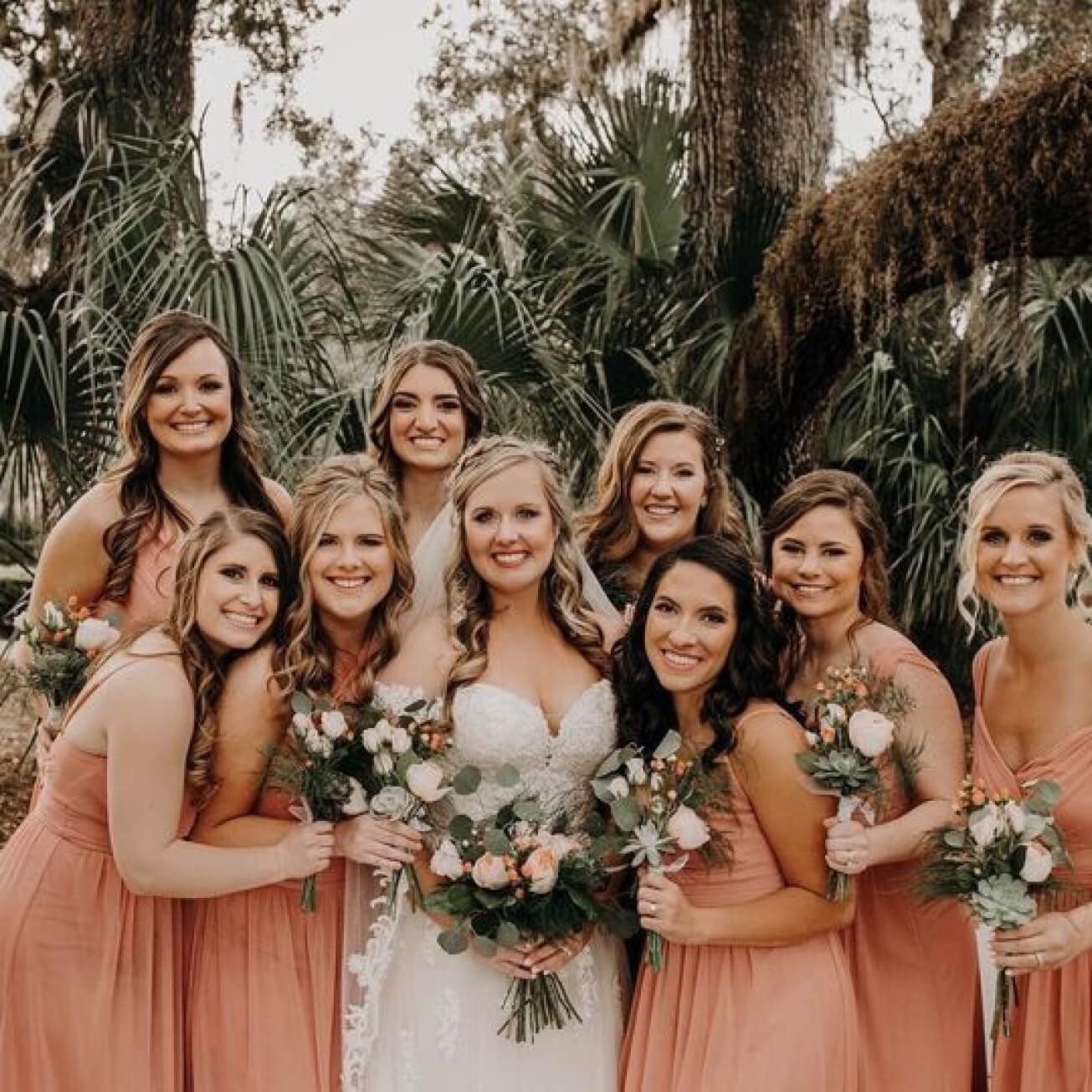 bride in a wedding dress standing with bridesmaids in orange dresses holding flower bouquets